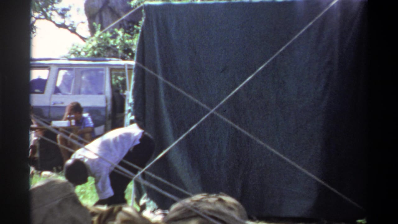 1969 Lagos 8mm frame showing a dark tent wall, crossed support lines, a bending figure, and part of a white van in the field.