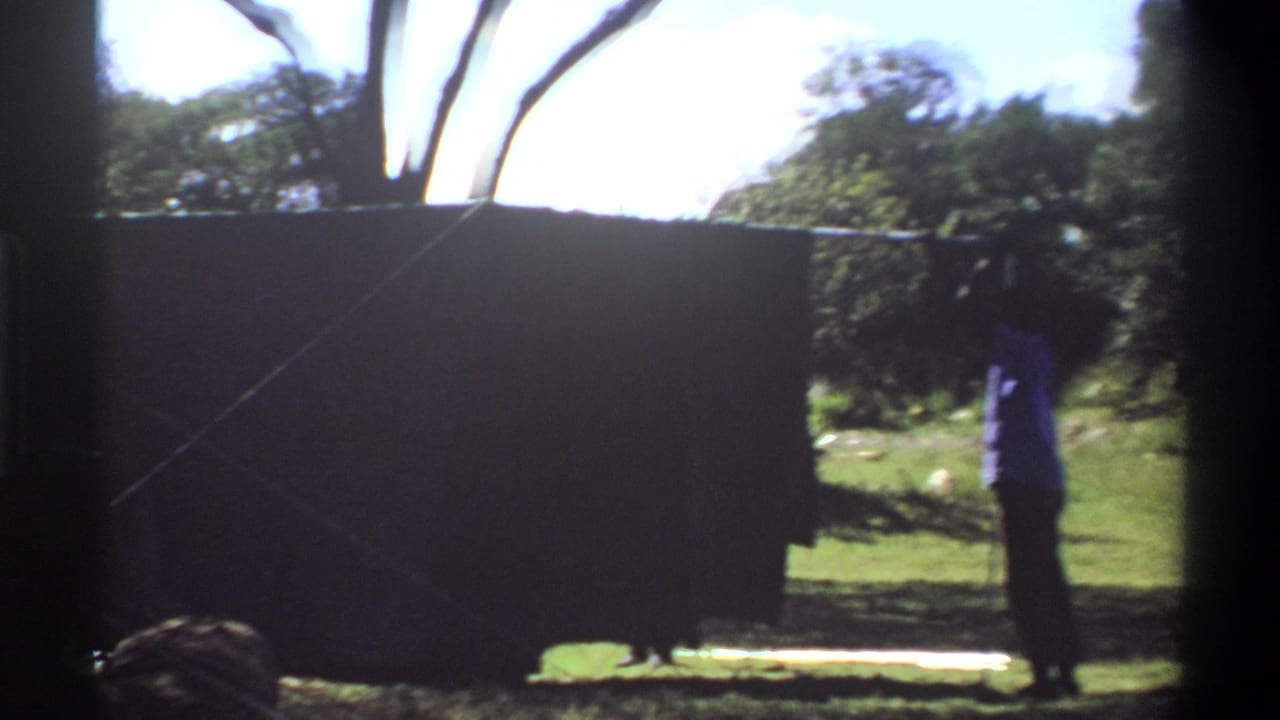 1969 Lagos frame with a large dark tent panel across the foreground and one person standing in the grass near trees.