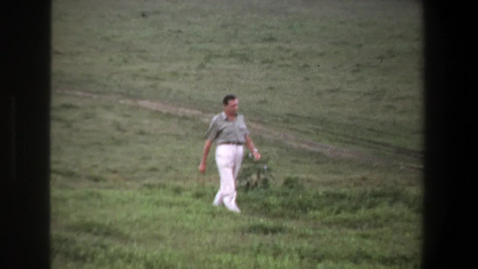 1969 Pretoria frame showing an adult man walking through grassland near a pale dirt track, with soft 8mm color and grain.