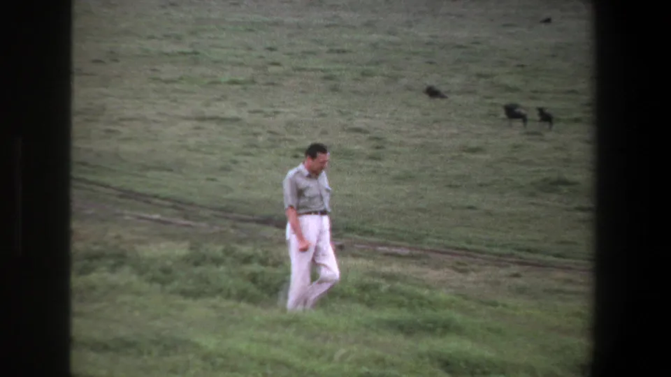 A distant adult man walks along the grassy slope near Pretoria, with 8mm grain and muted color visible in the frame.