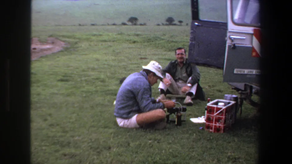 In the final frame, two men sit by equipment and a red cooler next to a parked vehicle in the grassy Pretoria setting.