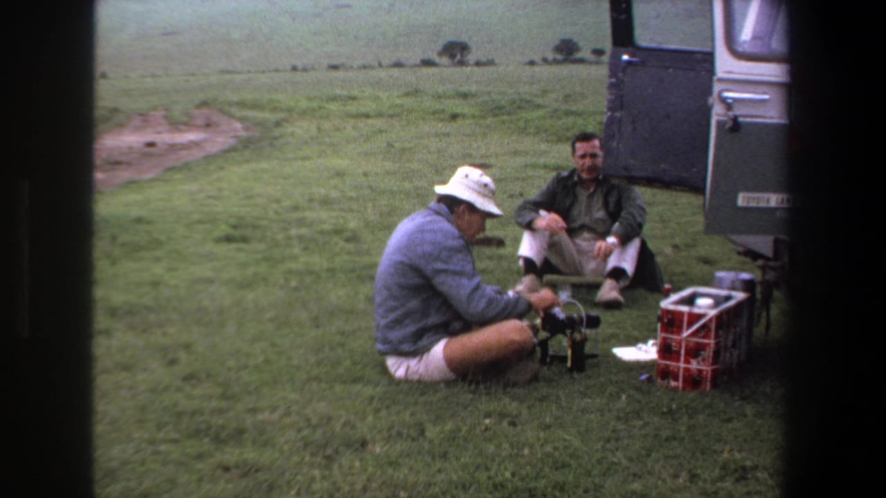 One man in a white hat works with small gear on the grass while another sits near the open rear doors of a vehicle in Pretoria, 1969.