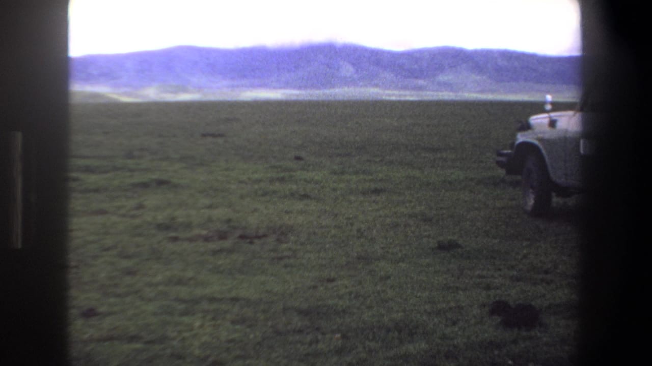 1969 Pretoria-area home-movie frame showing a grassy plain, distant hills, bright sky, and a partial parked truck.