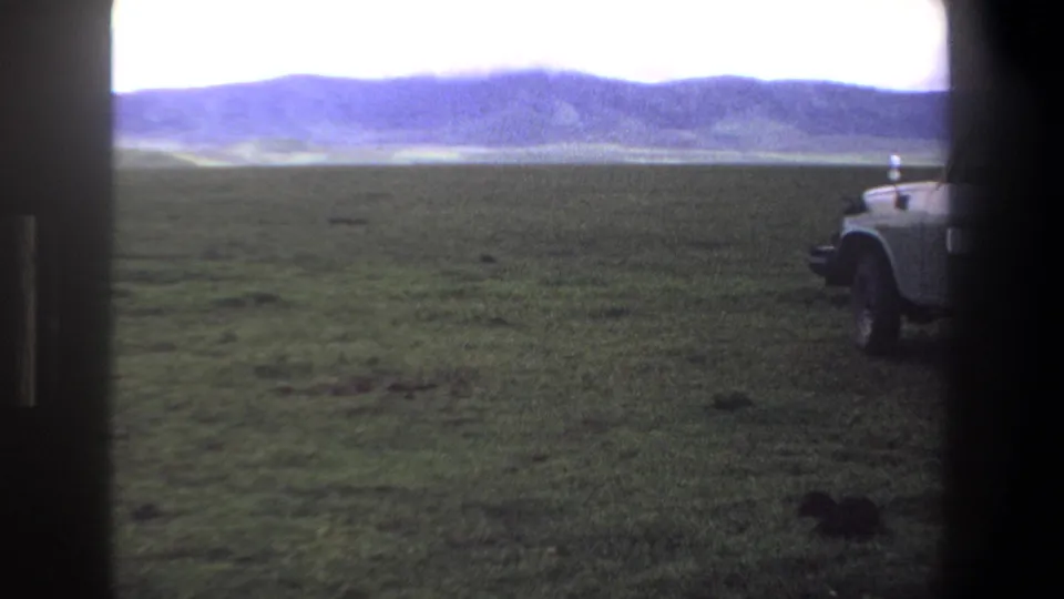 1969 Pretoria-area home-movie frame showing a grassy plain, distant hills, bright sky, and a partial parked truck.