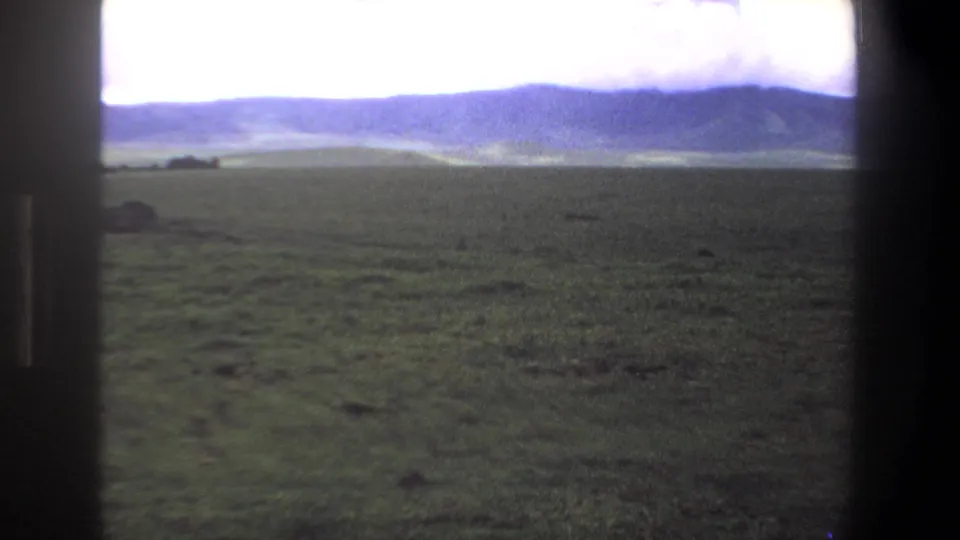 1969 Pretoria-area 8mm frame of an open grassy plain with blue distant hills and dark vertical framing at the sides.