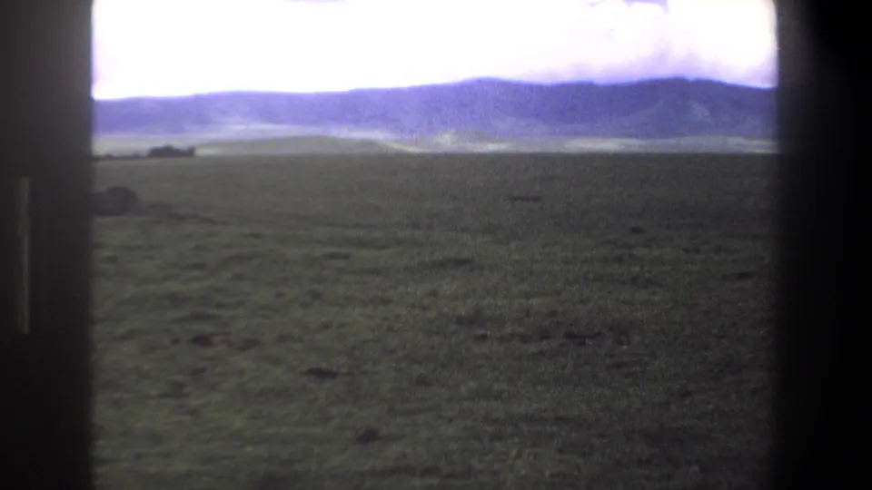 1969 Pretoria-area home-movie view across a grassy field toward low blue hills under a bright sky.