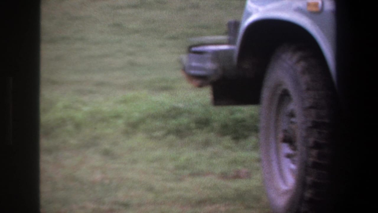 In Pretoria 1969 home-movie footage, an adult man appears beside a light-colored utility vehicle on a grassy field.