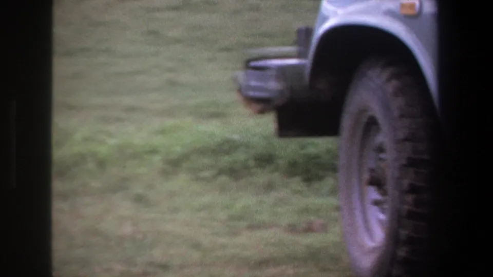 In Pretoria 1969 home-movie footage, an adult man appears beside a light-colored utility vehicle on a grassy field.