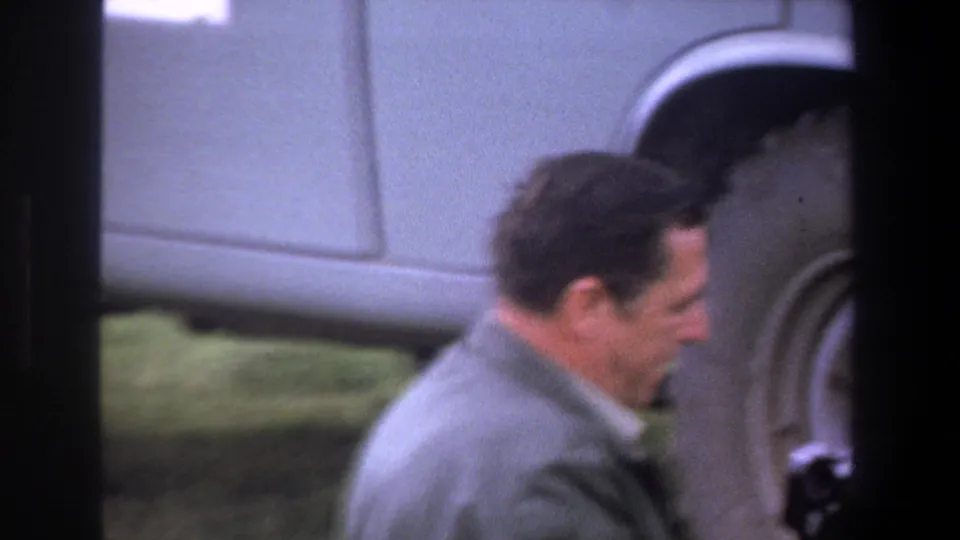 An adult man in profile stands near the large wheel of a light-colored utility vehicle in the Pretoria 1969 clip.