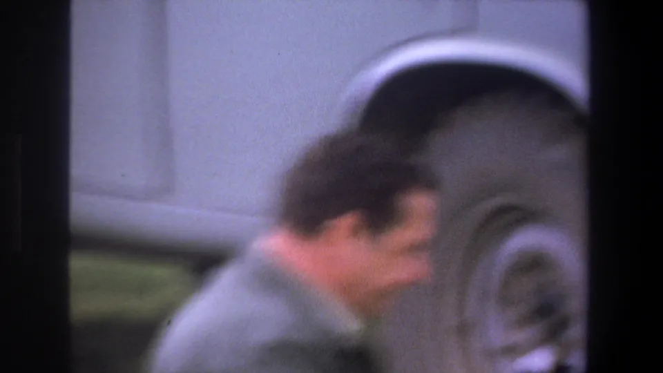 A blurred adult man moves across the foreground near a large wheel in this 1969 Pretoria home-movie frame.