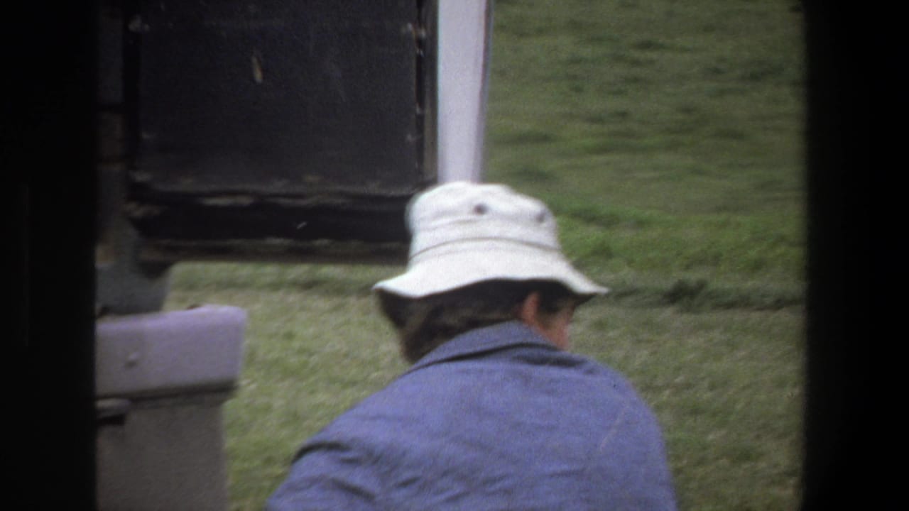 In 1969 Pretoria safari footage, a person in a white bucket hat and blue jacket looks out from a vehicle toward grassy terrain.