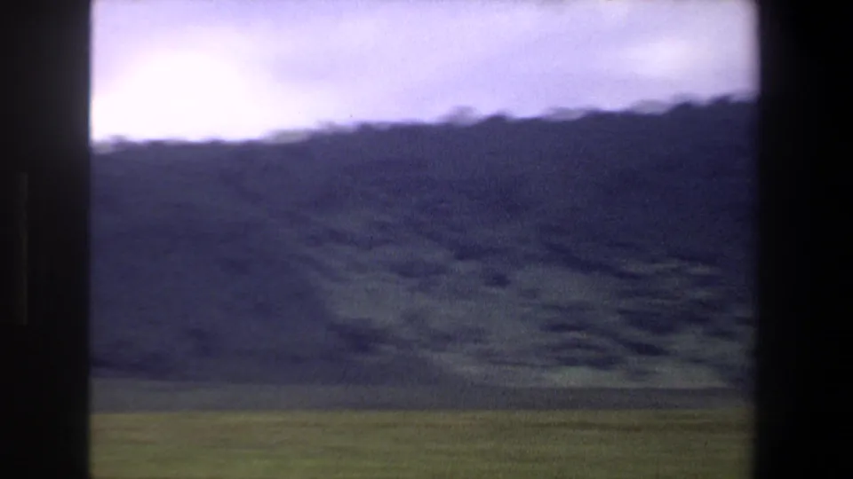 1969 Pretoria home-movie frame showing a green field and dark mountain slope beneath an overcast sky.