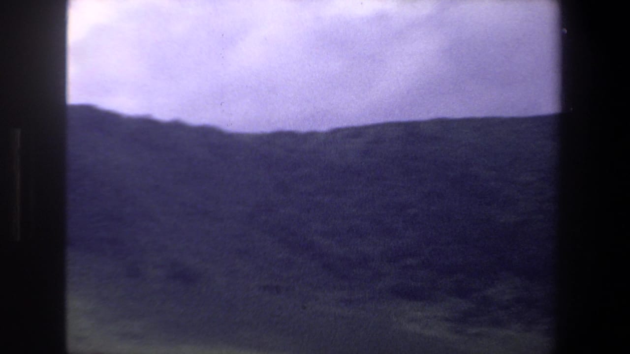 Dark mountain ridge and open field seen through heavy vertical film borders.
