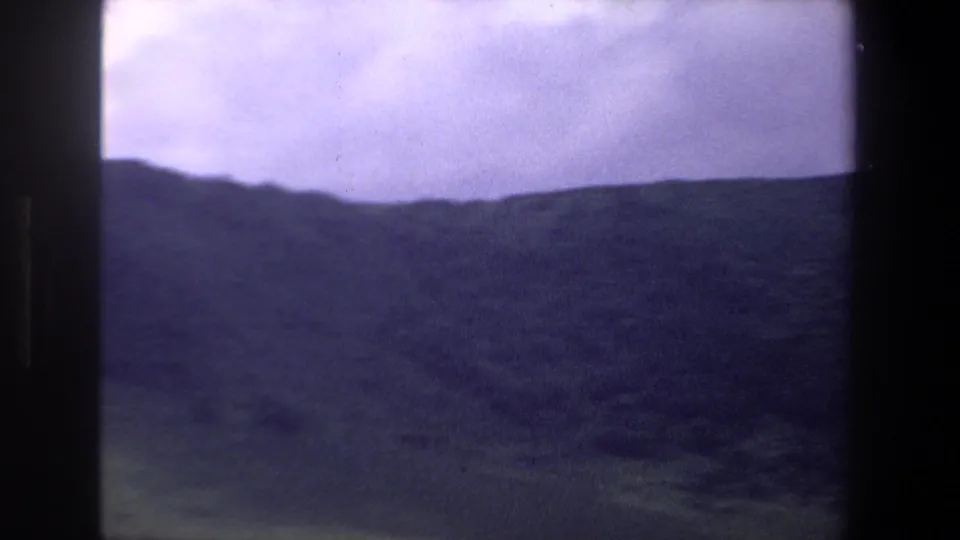 Pretoria-area 8mm frame with a broad dark hillside, grassy lower ground, and pale sky during a camera pan.