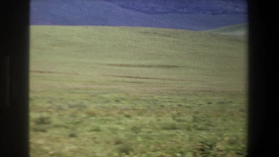 1969 Pretoria home-movie frame showing open green meadow, low dark hills, and a blue-purple sky through dark window or film edges.