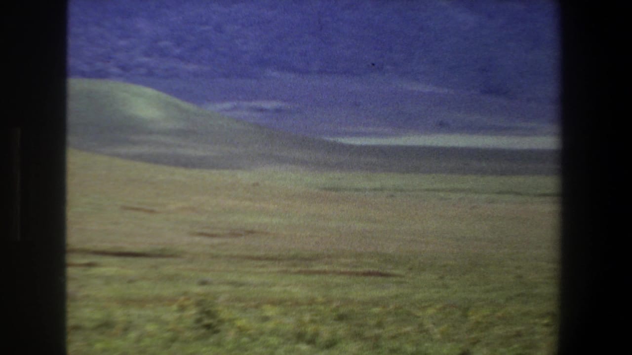 1969 Pretoria landscape view with rolling green grassland, distant dark ridges, and dark vertical borders from the filming setup.