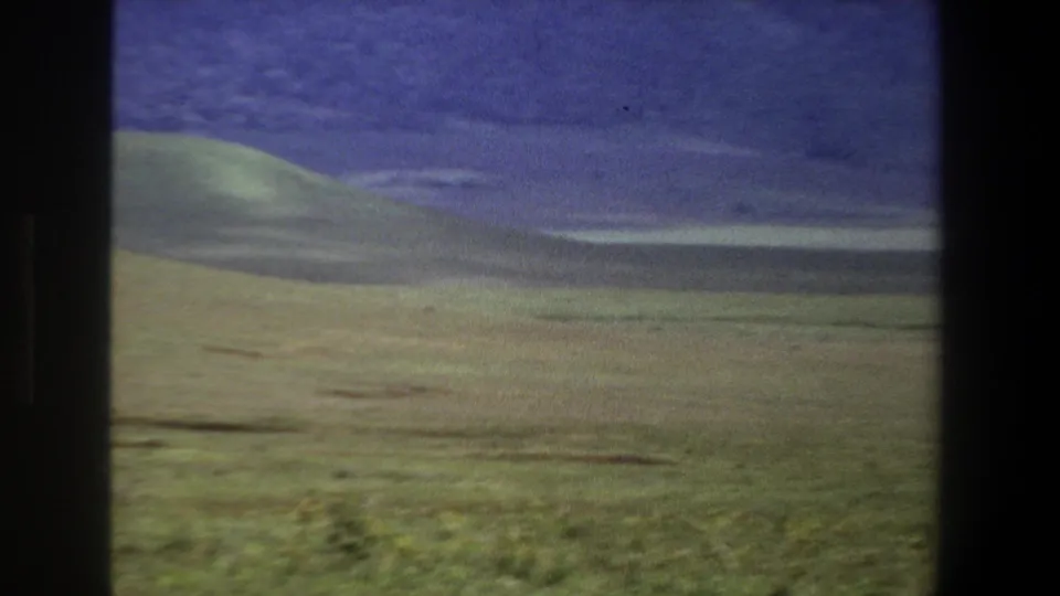 1969 Pretoria landscape view with rolling green grassland, distant dark ridges, and dark vertical borders from the filming setup.