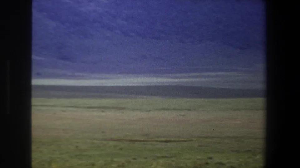 1969 Pretoria home-movie still showing a broad grassy plain, distant dark hillside, and visible film softness and color shift.