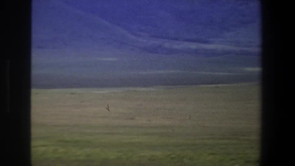 1969 Pretoria-area home-movie view of green open land and distant hills under heavy cloud, with soft 8mm color and dark frame edges.