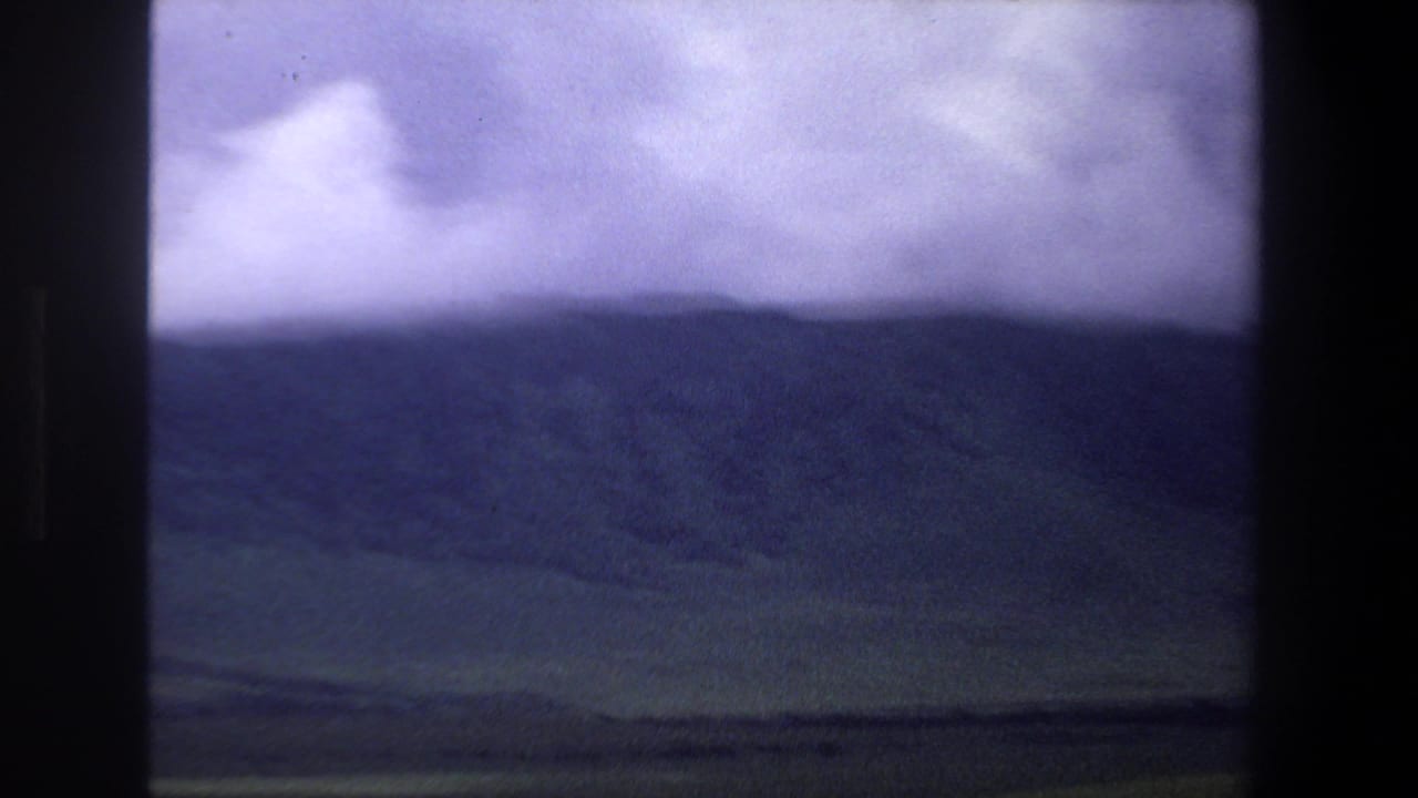Dark hillside and low cloud cover above a green valley, seen through film-frame borders.