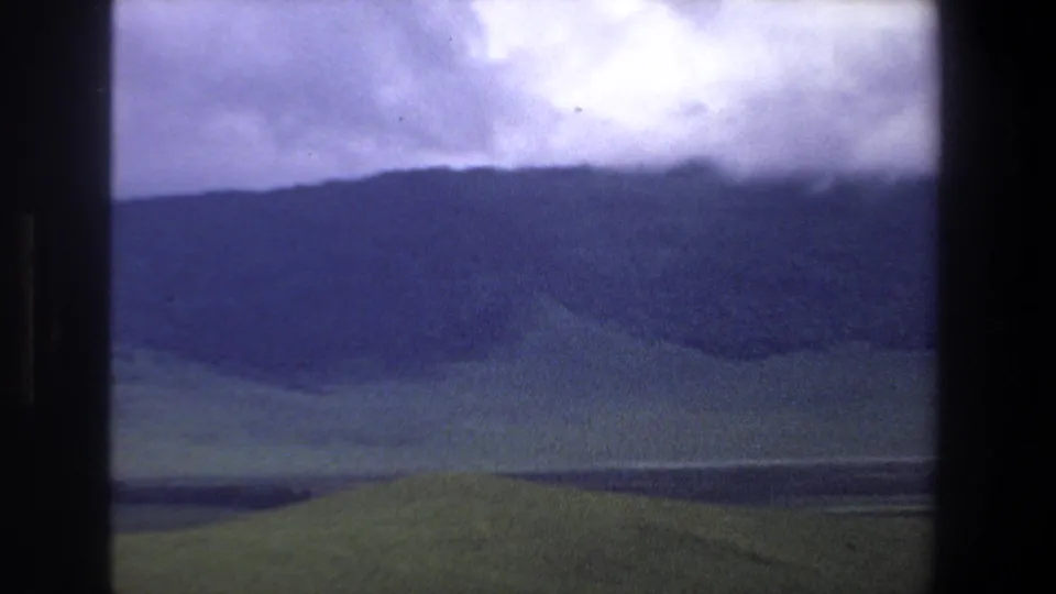 Vintage 8mm landscape frame from the Pretoria metadata location, showing cloud cover over hills and open green terrain.