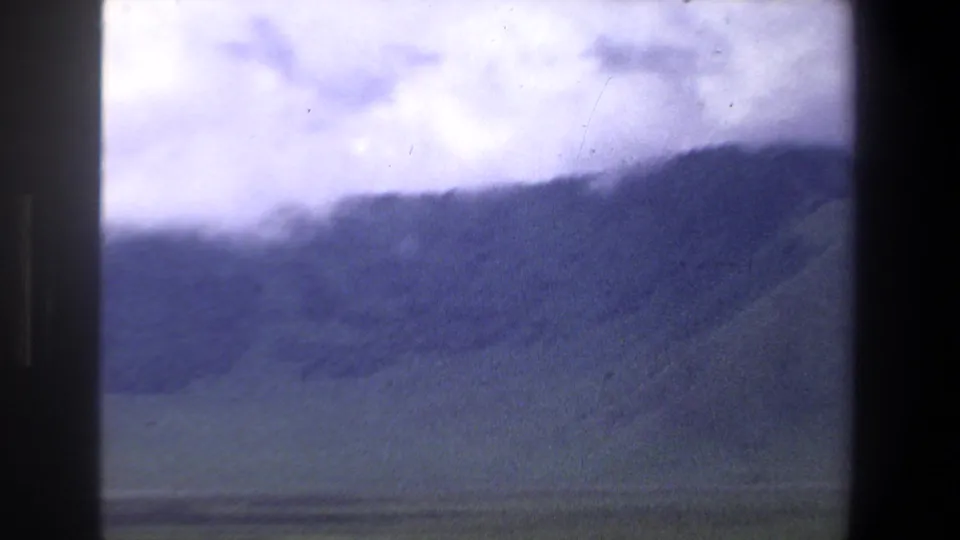 End frame of the 1969 Pretoria landscape pan, with rolling hills, muted green foreground, and bright clouded sky in 8mm texture.