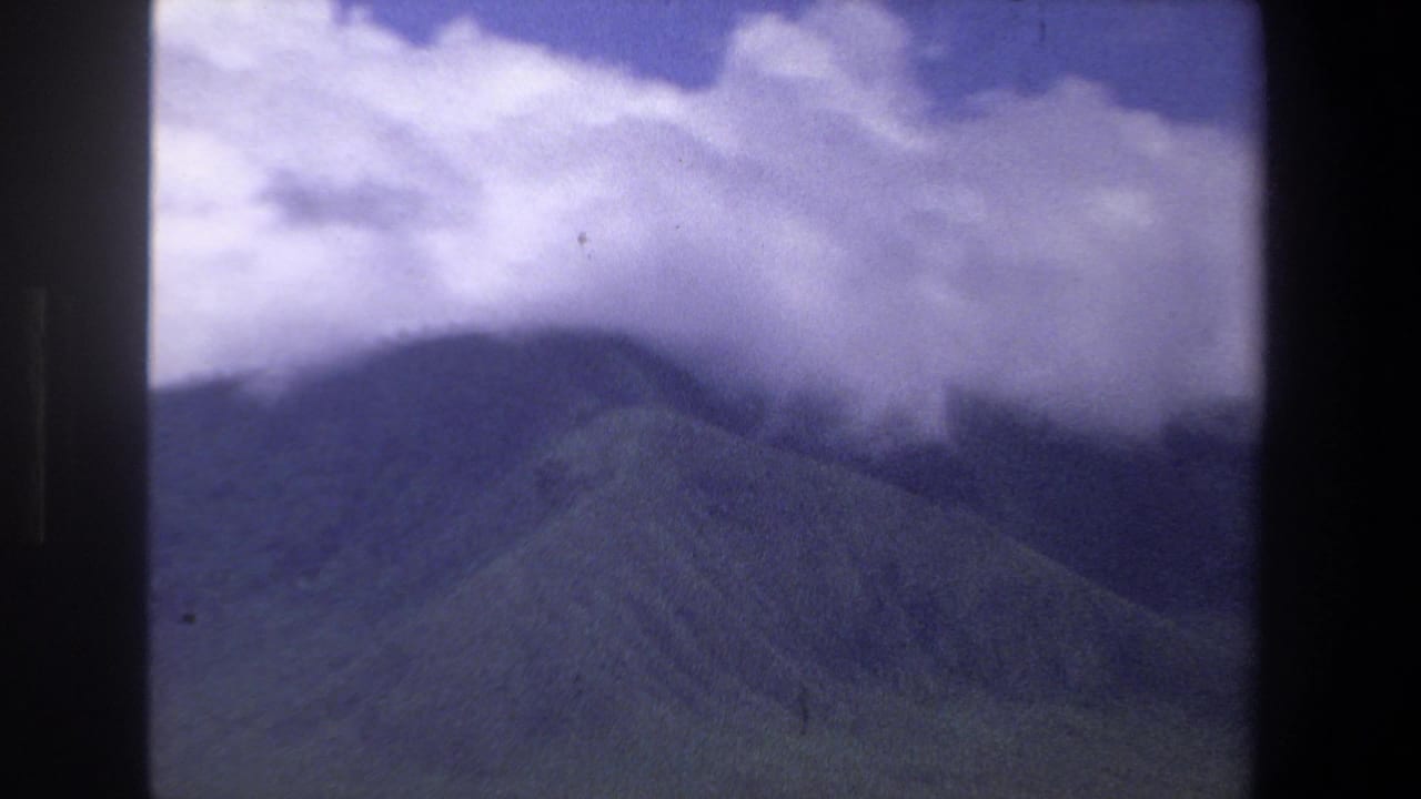 Clouds covering the top of a dark mountain range under a blue sky.
