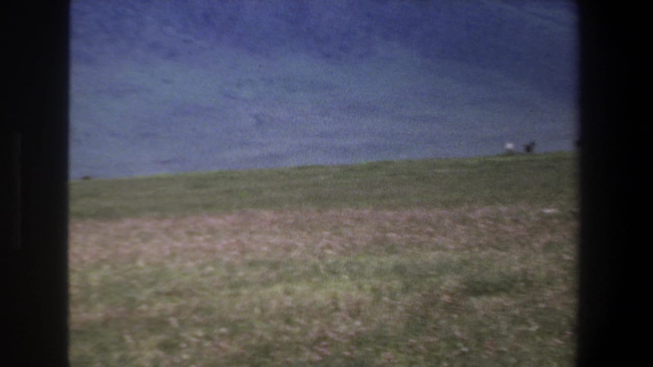 Grassy hillside with distant mountains and dark vertical film borders.