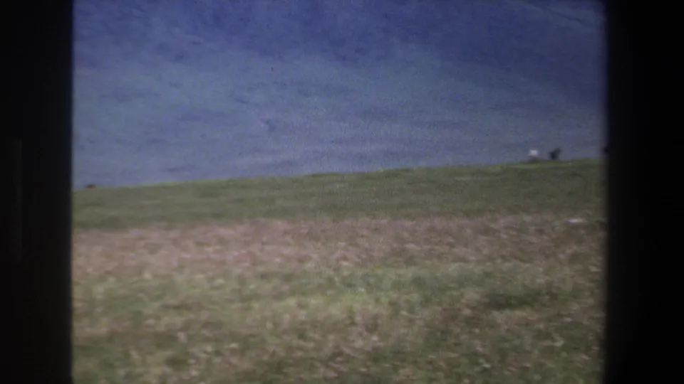 1969 Pretoria-area 8mm frame showing open grassland below blue-gray mountains, with dark borders across the view.