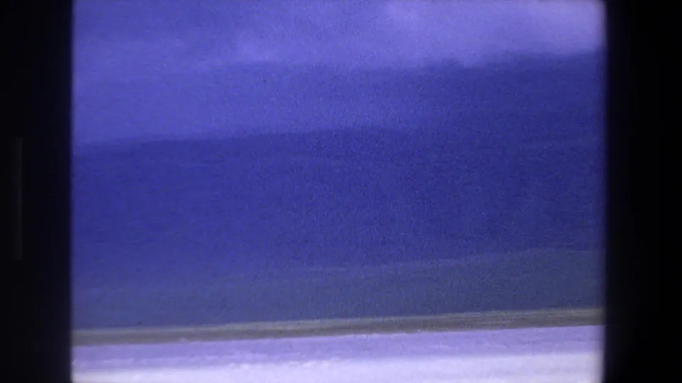 1969 Pretoria 8mm frame with a blue lake, faint shoreline, soft distant landforms, and heavy gate shadow at the frame edge.