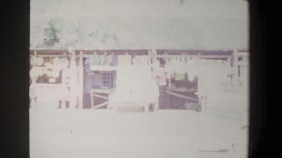 1969 Pretoria market frame showing overexposed stall fronts, hanging cloth or garments, wooden railings, and indistinct people in the aisle.