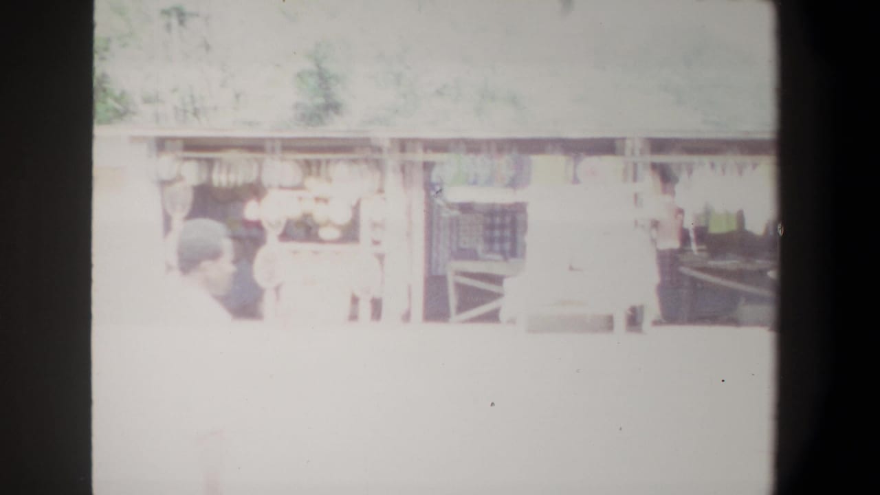 1969 Pretoria home-movie frame showing pedestrians near a long open-sided building, partly obscured by exposure bloom and film borders.