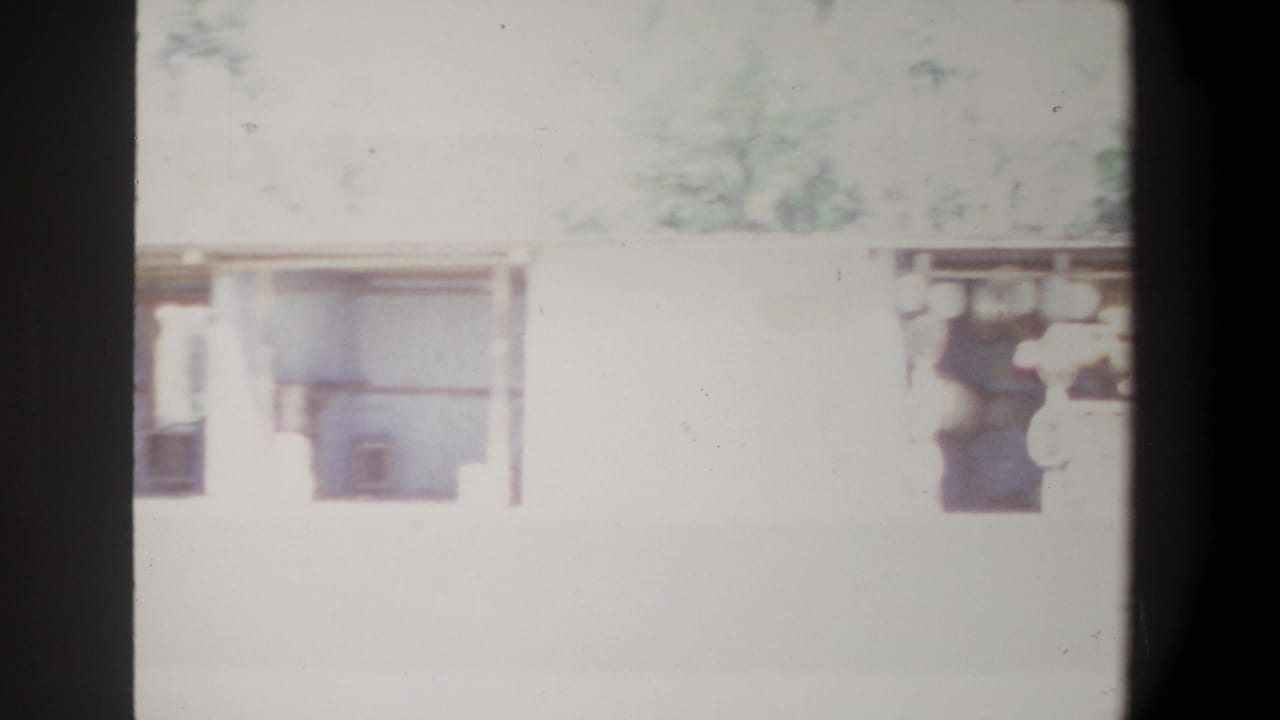 Long pale building with open bays and dark film borders, with faint figures near the structure.