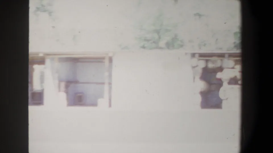 1969 Pretoria frame with a pale open-sided structure and indistinct pedestrians, softened by faded color and strong overexposure.
