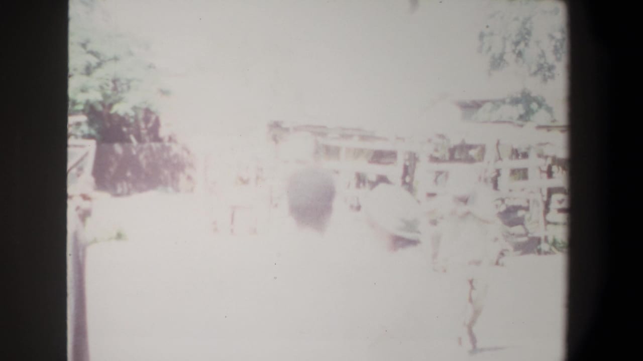 Highly overexposed 8mm frame from the supplied Pretoria 1969 clip, showing a market area with awnings and indistinct people.