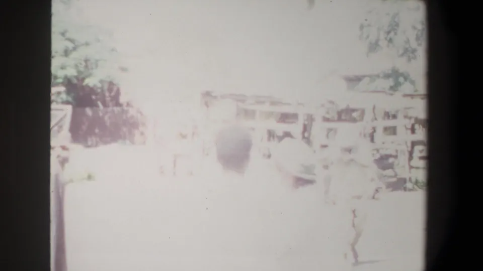 Highly overexposed 8mm frame from the supplied Pretoria 1969 clip, showing a market area with awnings and indistinct people.