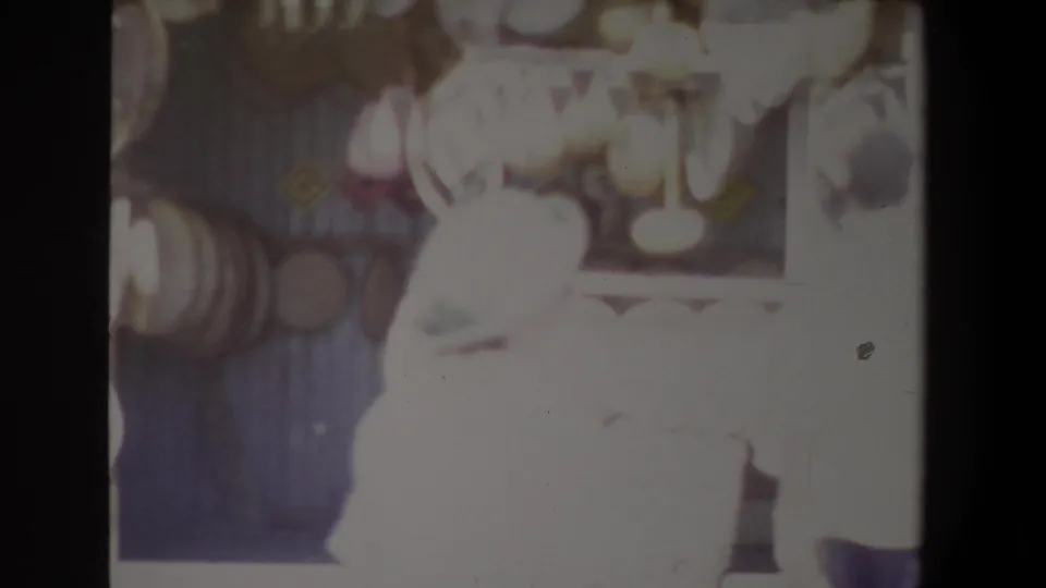 Soft 8mm frame showing figures near a stall with hanging items and a very bright foreground figure.