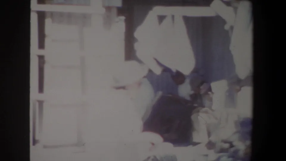 1969 Pretoria market footage shows adults near a textile stall, with strong overexposure obscuring some facial detail.