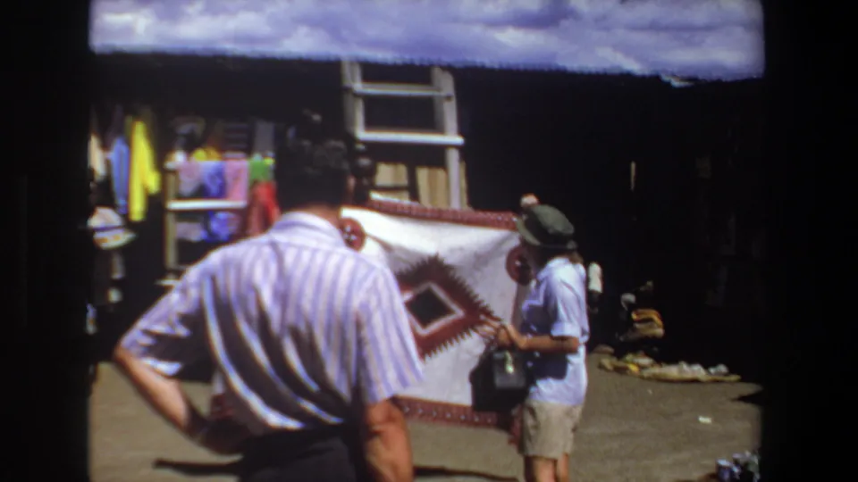 1969 Pretoria market frame with a striped-shirt shopper seen from behind as a vendor presents a large geometric blanket.