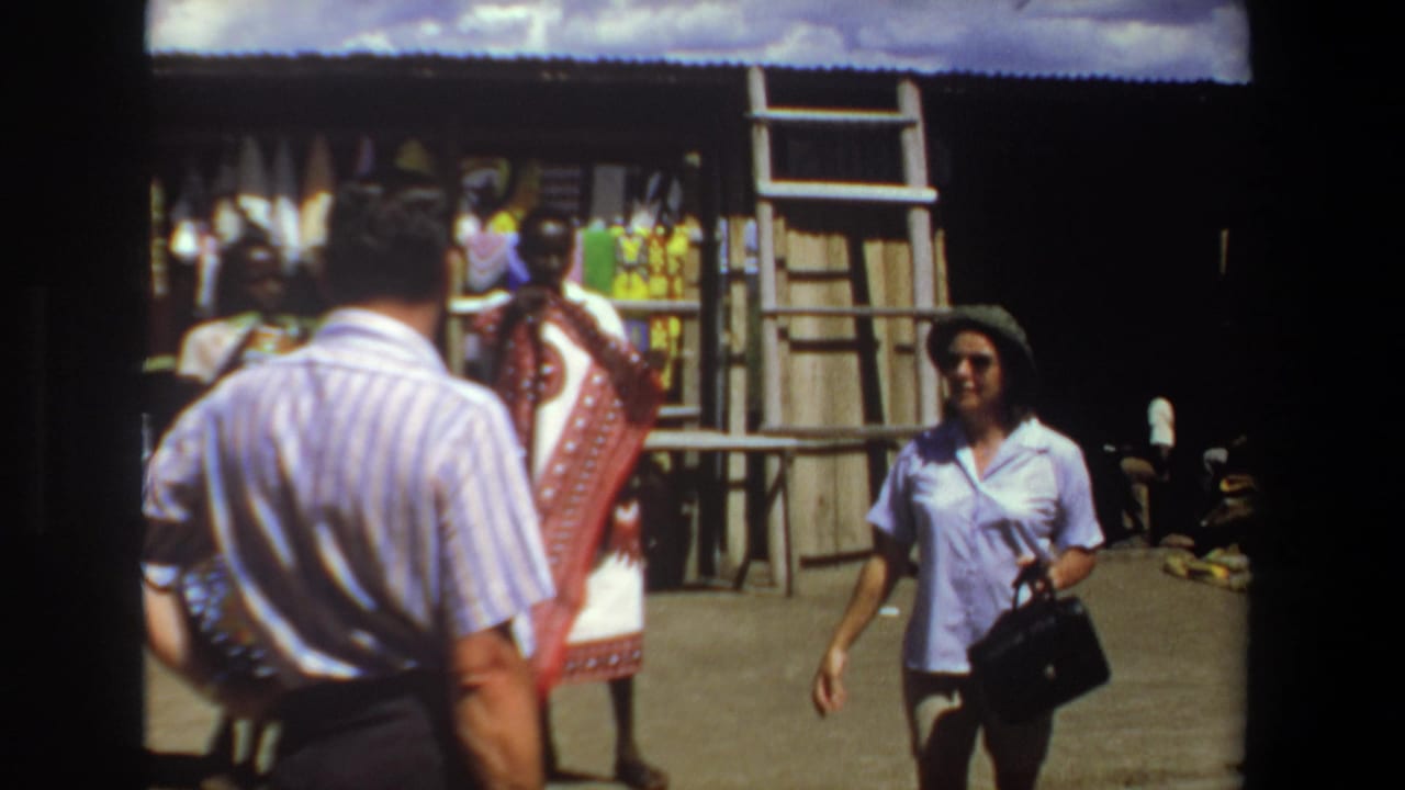 1969 Pretoria market frame with a woman carrying a handbag walking near a textile vendor and fabric stall.