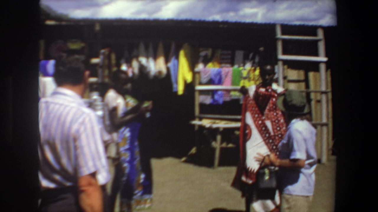 Visitors browse a shaded market stall with hanging textiles and colorful fabrics.