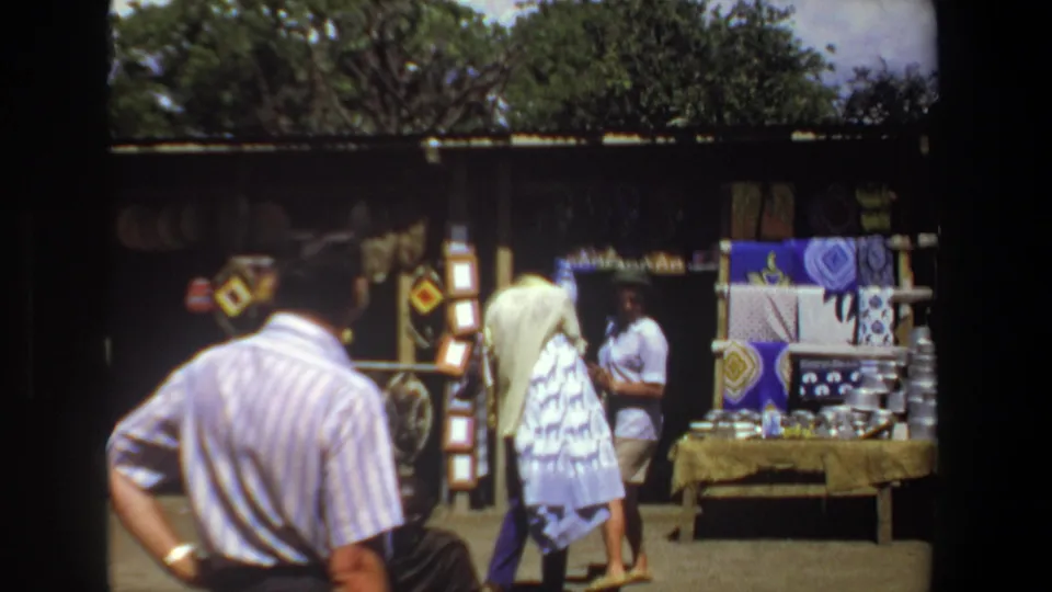 1969 Pretoria open-air market frame with a visitor in the foreground and craft goods arranged under a shaded stall.