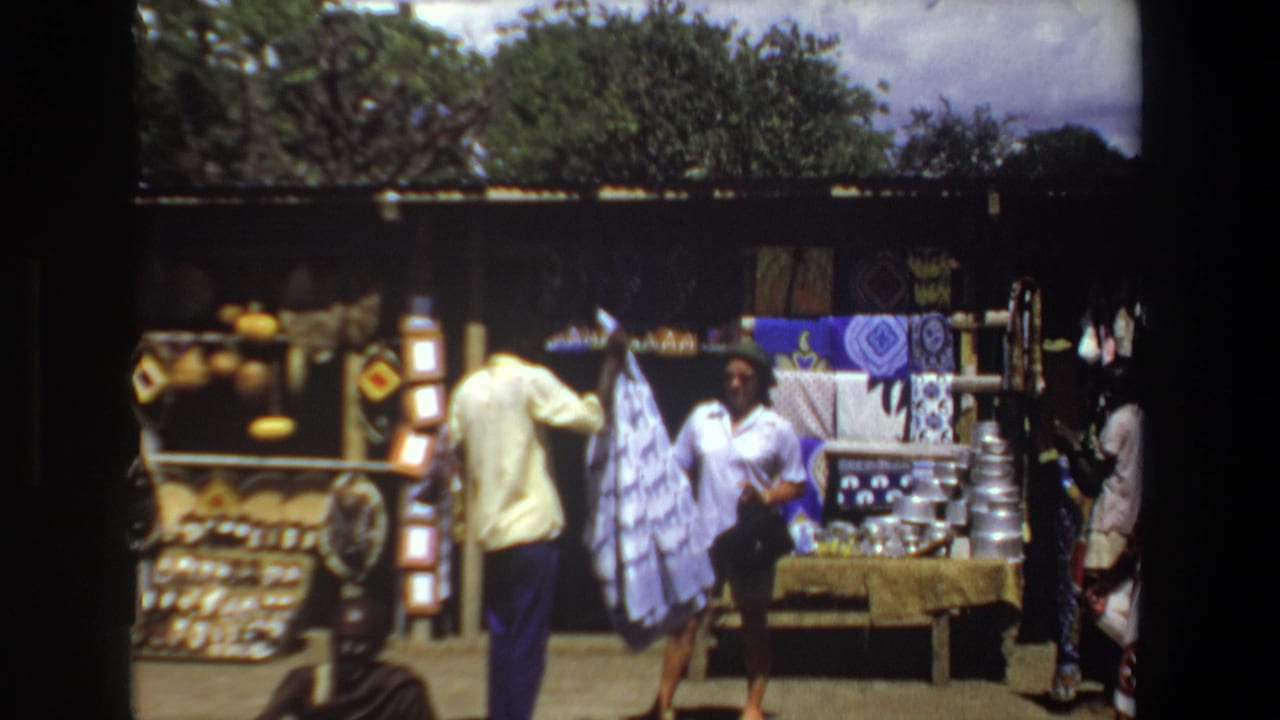Pretoria, South Africa home-movie frame from 1969 showing adult shoppers near woven baskets and patterned textiles at an outdoor market stall.