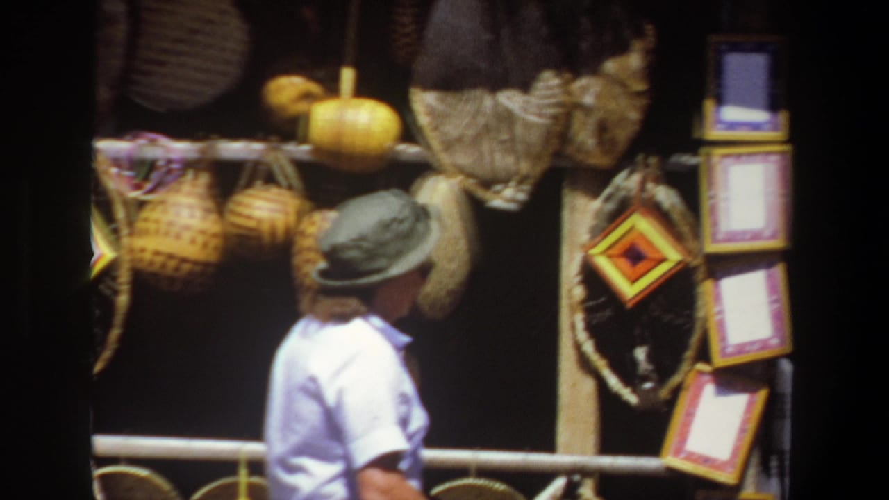 The 1969 Pretoria market view shows the woman turned toward a display of woven baskets, yellow gourds and framed decorative items.