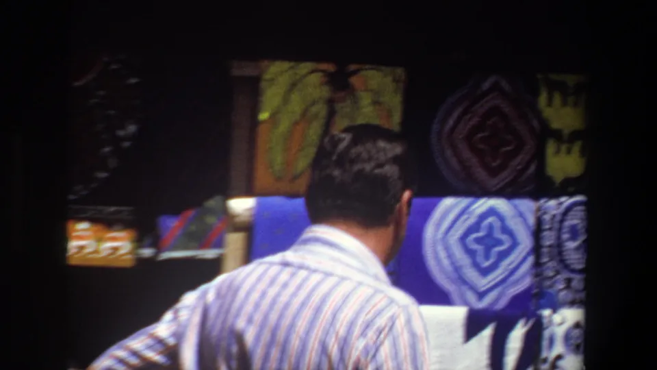 The final frame shows the striped-shirt man from behind near blue and patterned textiles displayed in the Pretoria market stall.