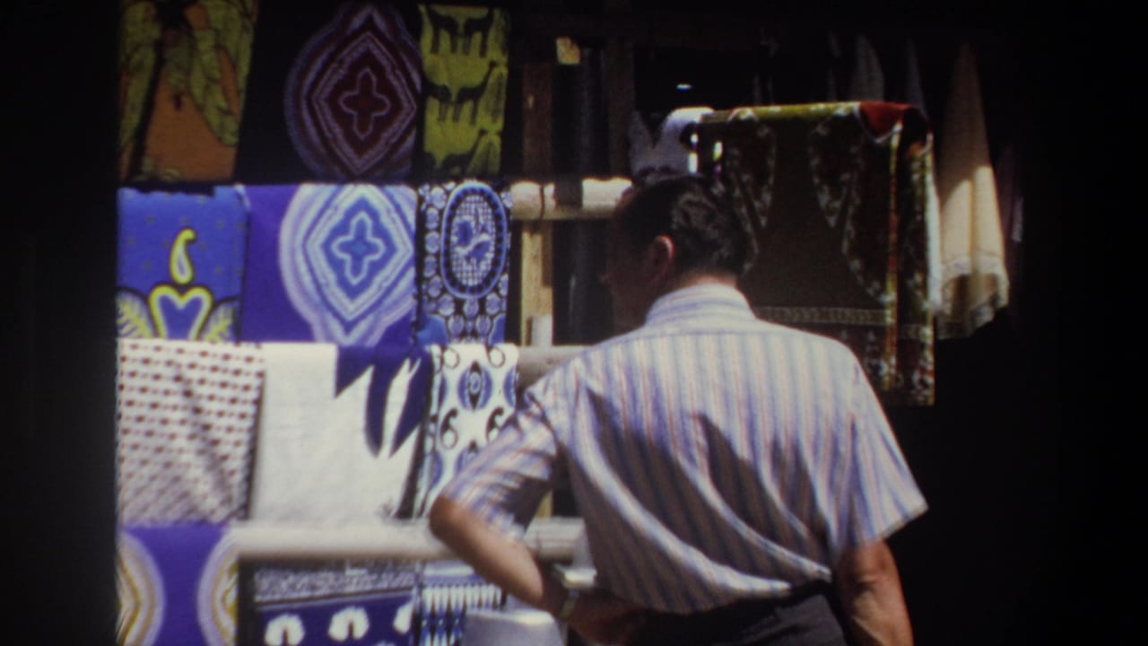 Man in a striped shirt stands with one hand on his hip beside a textile display.