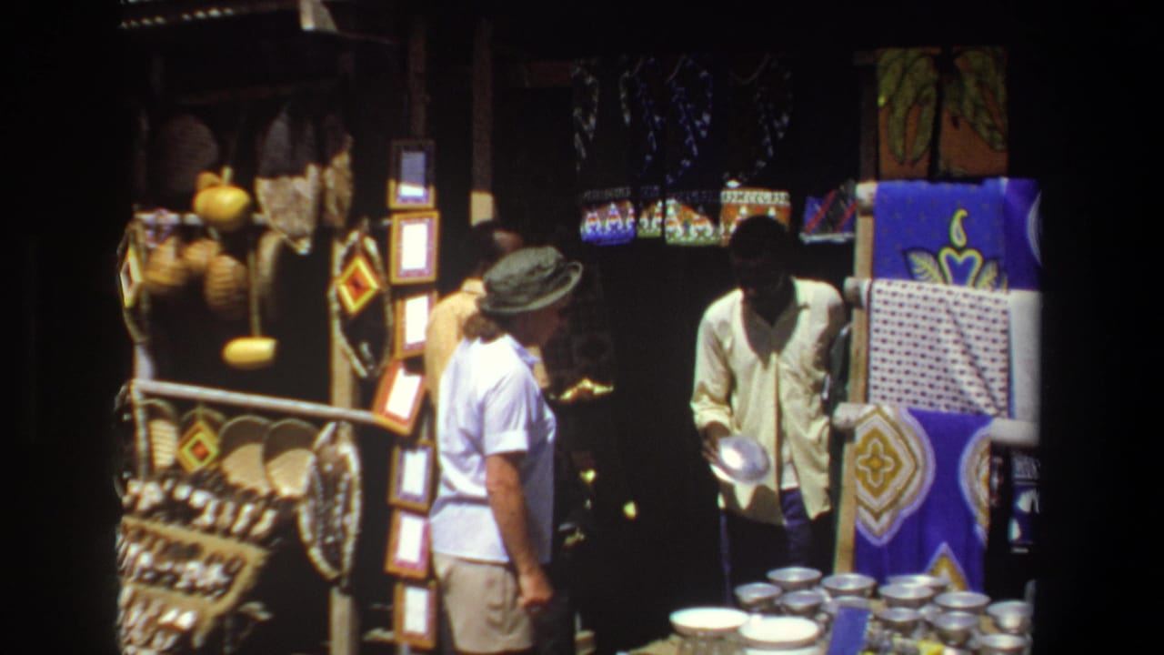 Woman faces a vendor holding a bowl beside stacks of metal dishes and colorful hanging textiles.