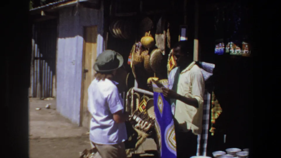 The 1969 Pretoria market scene shows a tourist and vendor in conversation beside baskets, textiles, and small white bowls.