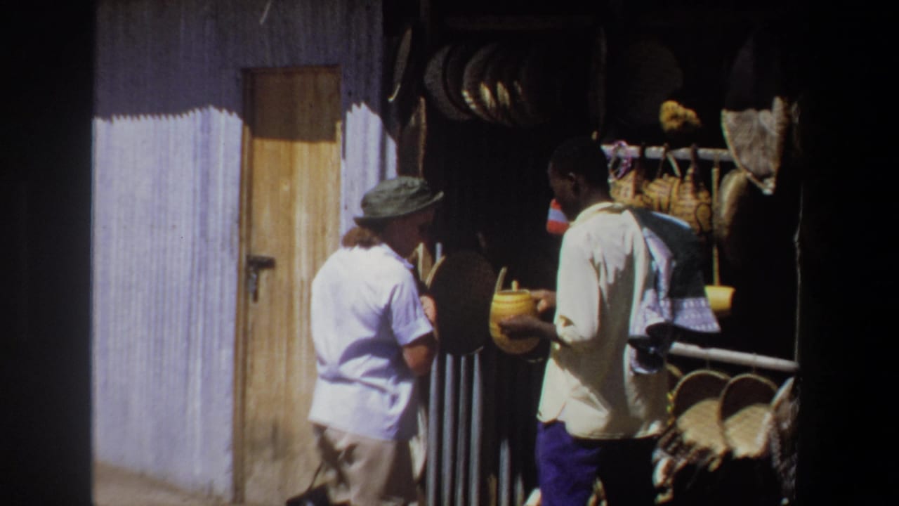 Vendor holds a yellow container while a woman in a hat stands near baskets at the stall.