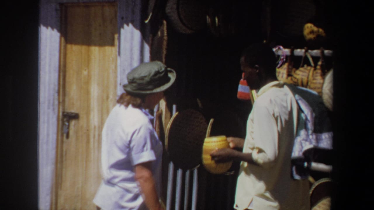 Vendor and woman stand beside a stall with baskets and hanging handmade goods.